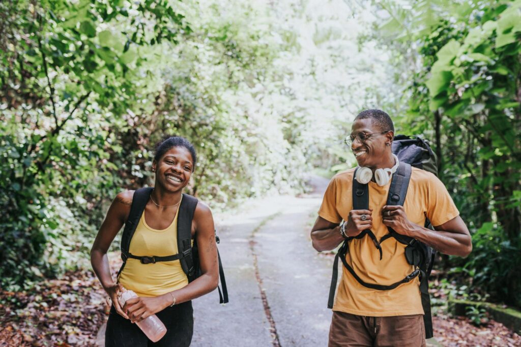 Two hikers with rucksacks smiling whilst walking on a forest trail.